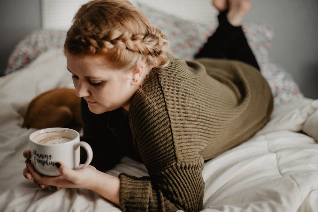 woman laying on bed with a cup of coffee
