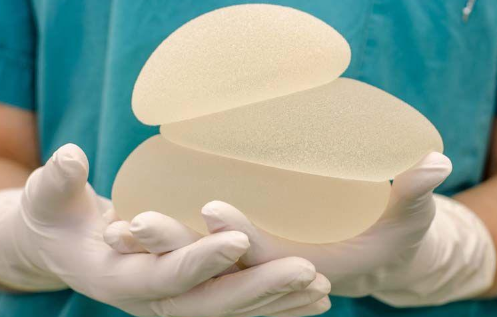 gloved hands holding breast implants