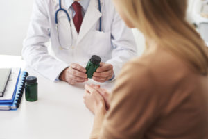 doctor in a white coat holding a green medicine bottle, sitting across from a patient