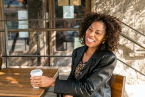 Black woman sitting at table with to-go coffee, laughing